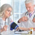 A stroke kockázatainak csökkentése foláttal és egyéb B-vitaminnal Idősebb orvos egy idős női páciens vérnyomását méri, előttük az asztalon gyógyszerek.