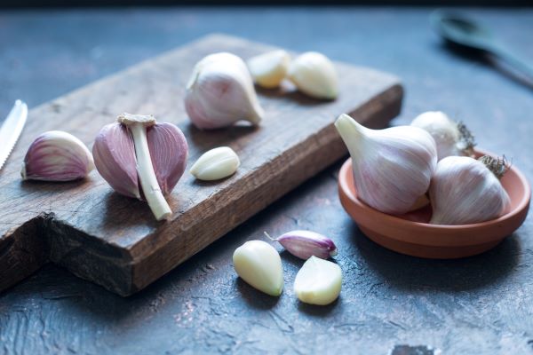 Vágódeszkán és kis tálban egész és gerezd fokhagymák.