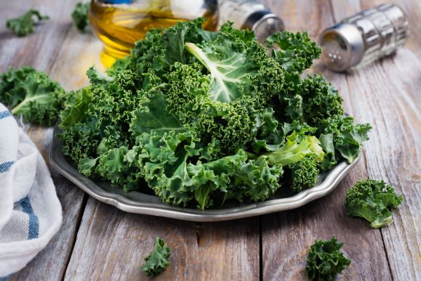 Faasztalon tányéron kelkáposzta-levelek, háttérben olívaolaj, só- és borstartó.