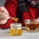 Valaki sállal a nyakában mézet tesz a teájába.