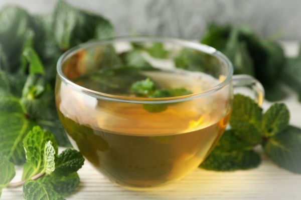 Üvegcsészében tea, körülötte mentalevelek.