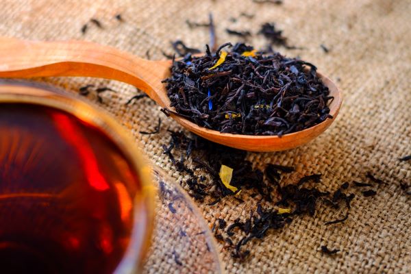 Egy csésze tea mellett fakanálban szárított feketetea-levelek.