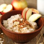 A zabkása egészségügyi előnyei – miért fogyasszuk reggelire? – 2. rész Egy tálban zabkása, rajta dió és almaszeletek, körülötte fahéjrudak, almák, dió, mazsola, egy pohár tej.