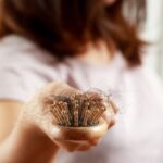 Nő a hajszálakkal teli hajkeféjét tartja a kamera elé.