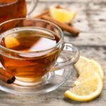 Üvegcsészében tea, mellette fahéjrúd és citromkarikák.