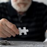 Idős férfi kirakózik, kezében puzzle-darab.