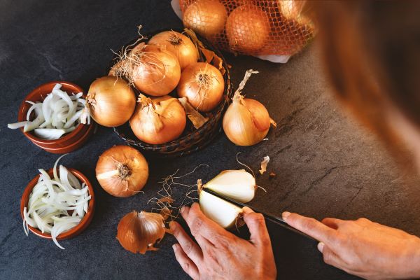 Valaki hagymát vág egy sötét konyhapulton.