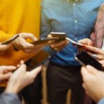 Fiatalok állnak körben mobiltelefonnal a kezükben.