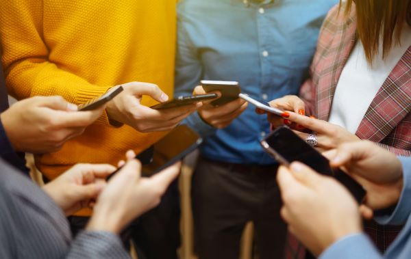 Fiatalok állnak körben mobiltelefonnal a kezükben.