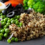 Szürke tányéron főtt quinoa, zöldborsó, szeletelt olajbogyó, főtt tojás, brokkoli, lila hagyma.