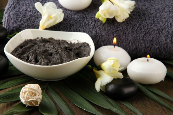 Fehér kerámiatálban szürke iszap, mögötte szürke törülköző, mellette két fehér mécses, fehér virágok.