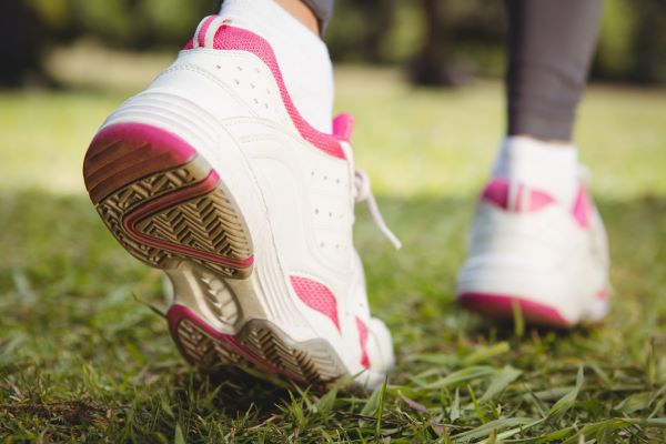 Nő sportcipőben gyalogol, a lábait látjuk közeli fotón, ahogy lép.