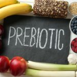 Fehér faasztalon különböző élelmiszerek, középen fekete táblán krétafelirat: "prebiotic".