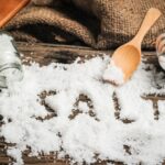 Faasztalon kiszórva sok durva szemcséjű só, "beleírva" a "salt" szó, mellette felborult sótartó, fakanál.