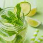 Közeli fotó mentás vízről egy füles csavaros üvegben, mellette lime és szívószál.
