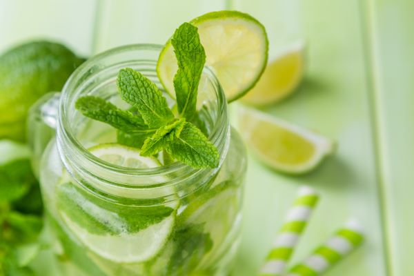 Közeli fotó mentás vízről egy füles csavaros üvegben, mellette lime és szívószál.