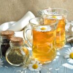 Faasztalon két pohár tea kamillavirággal, mellette három kis üvegben szárított gyógynövények.