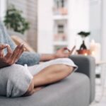 Nő ül a kanapén lótuszülésben, és meditál.