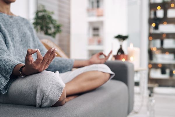 Nő ül a kanapén lótuszülésben, és meditál.