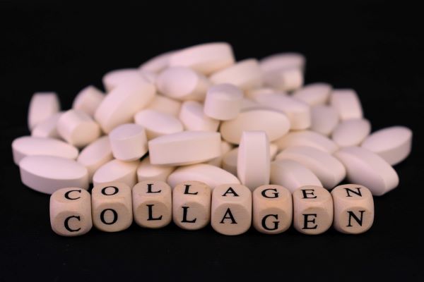 Fekete háttéren fehér ovális tabletták, elöl fa betűkockákból kirakva a "collagen" szó.