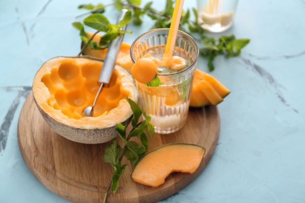 Kerek vágódeszkán sárgadinnye és egy pohár limonádé sárgadinnyegolyókkal és mentalevéllel.