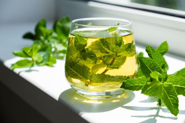 Ablakpárkányban egy pohár mentatea, benne és mellette mentalevelek.
