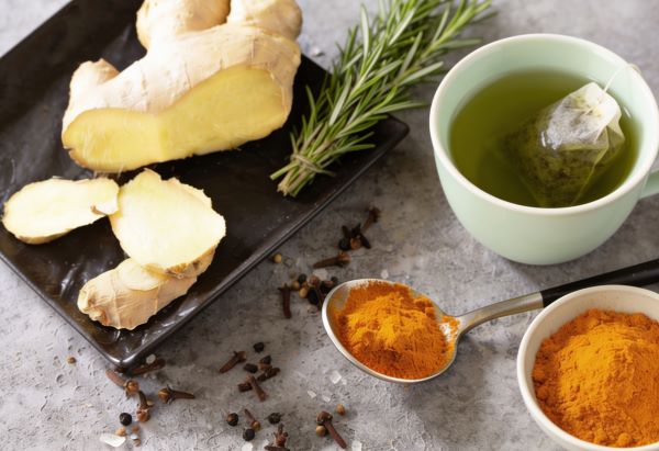 Márványos felületen gyömbér, kurkuma, rozmaring, szegfűszeg, egy csésze zöld tea.