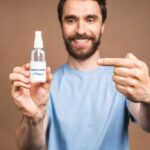 Szakállas orvos kék öltözetben egy magnéziumolaj spray-t tart a kezében.