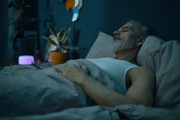 Idősebb, szakállas férfi alszik az ágyban éjjel.