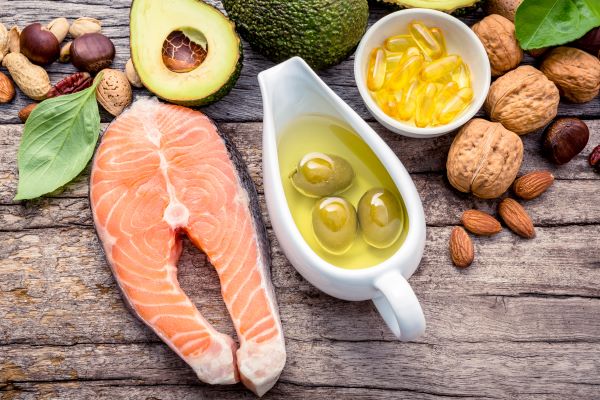 Faasztalon felülnézetben: halszelet, avokádó, diófélék, olívaolaj, olajbogyó, omega-3 kapszulák.