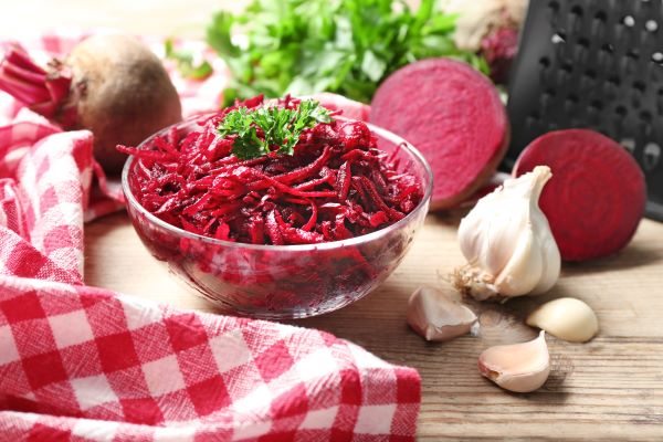 Üvegtálban reszelt cékla, mellette fokhagyma, cékla, reszelő, piros kockás konyharuha.