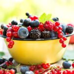 Sárga tálban vegyes bogyós gyümölcsök: szeder, ribizli, áfonya, málna.