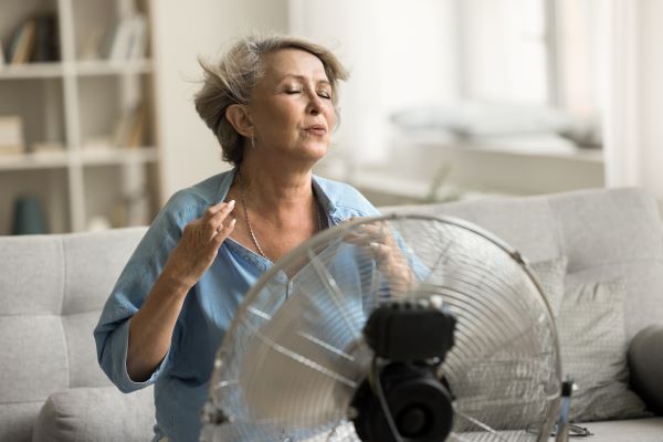 Középkorú nő ül a kanapén a ventilátor előtt.