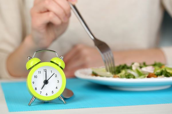 Nő salátát eszik, előtte egy sárga ébresztőóra.