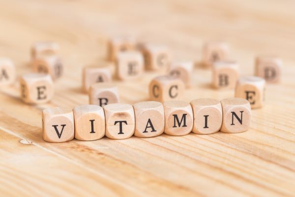 Faasztalon kis betűkockákból kirakva a "vitamin" szó, mögötte elszórtan különböző betűkockák: A, B, C, D, E.