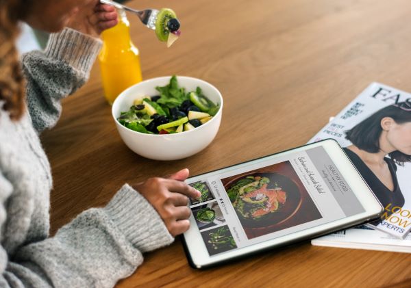 Nő salátás eszik, miközben egy tableten egészséges ételeket nézeget.