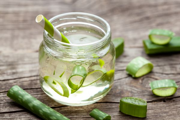 Faasztalon egy kis befőttesüvegben Aloe vera gél szívószállal, benne és körülötte Aloe vera darabok.