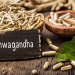Faasztalon kosárkában ashwagandha gyökér, fatálban kapszulák, előtte fatábla "Ashwagandha" felirattal.