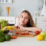 Az egészséges étel is mérgezhet – amikor a túlzás válik problémává Fiatal nő a konyhában, előtte a pulton zöldségek, gyümölcsök és mérőszalag.