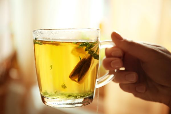 Női kézben egy pohár tea teafilterrel és gyógynövénnyel.